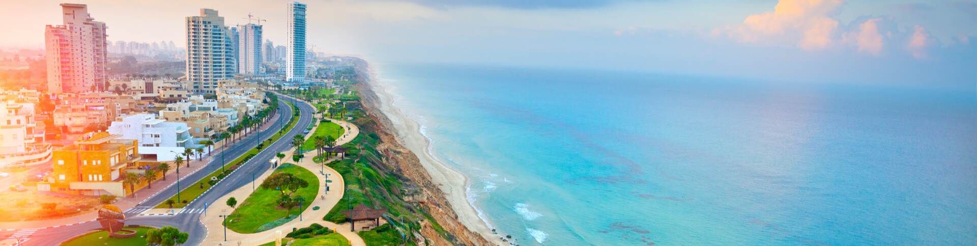 תצפית אווירית של קו החוף של נתניה בשעת השקיעה. בצד נראים בנייני מגורים גבוהים, כביש רחב וטיילת ירוקה