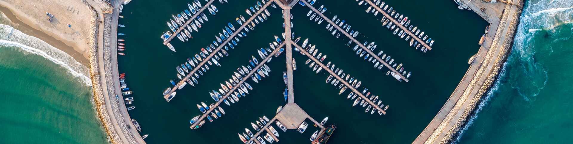 מבט אווירי על המרינה באשדוד, עם רציפים המסודרים בצורת מניפה ובהם עוגנות עשרות סירות ויאכטות